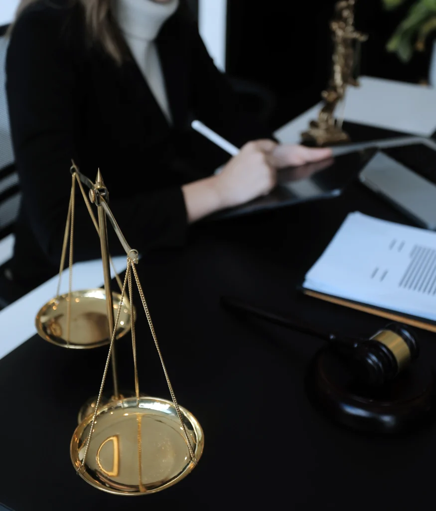 Professional attorney reviewing legal contract documents with golden scales of justice and wooden gavel on desk during client consultation